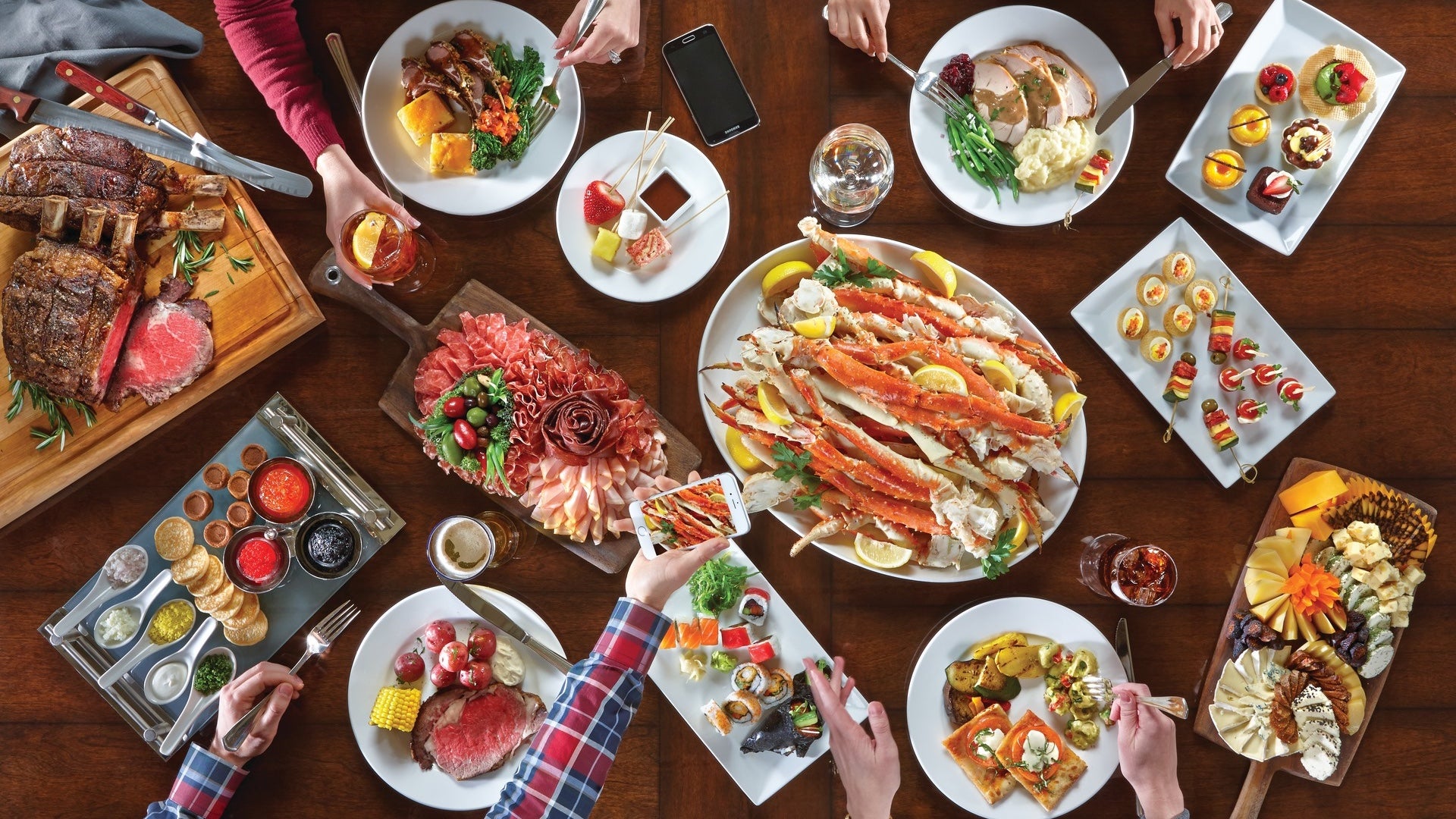 Several plates filled with food and hands reaching in to fill their dinner plates